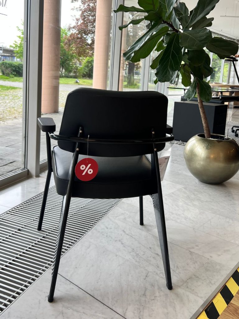 Black chair with a red percentage-off tag hanging from the backrest in a bright showroom by a window.
