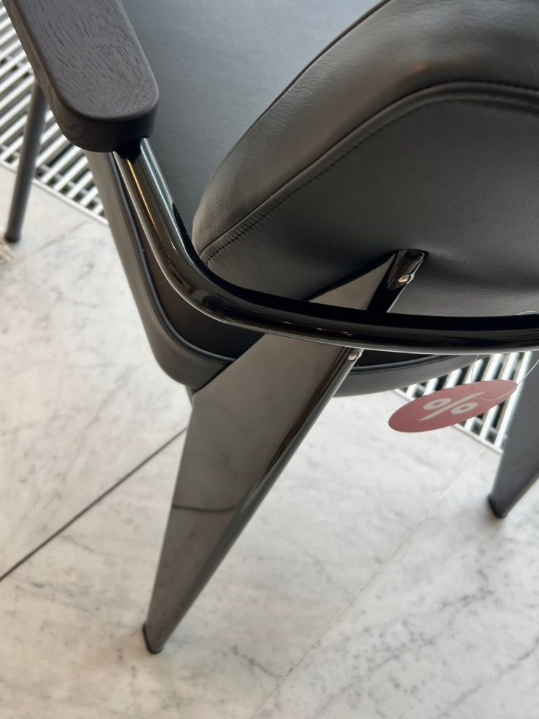 Close-up of a black-framed chair with a gray padded seat, featuring a pink discount tag hanging from the leg.