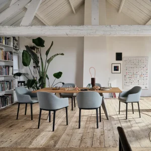 Loft-style dining room with a wooden table, six gray chairs, and a tall houseplant in the background.