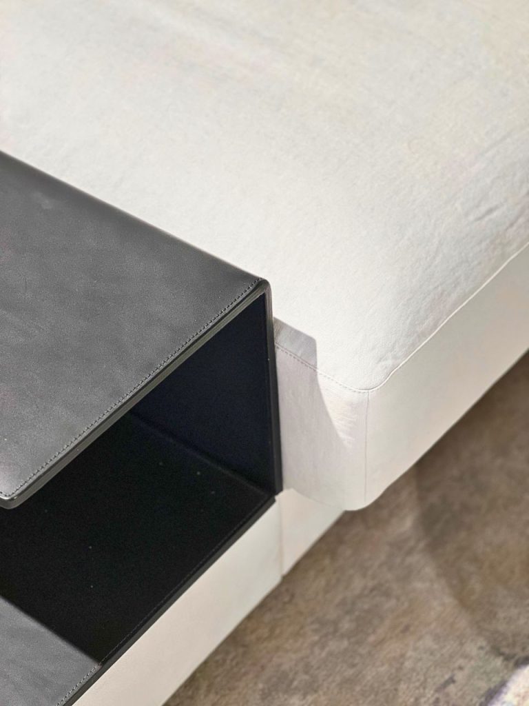 Black open storage box with an empty interior placed beside a light gray upholstered sofa/ottoman.