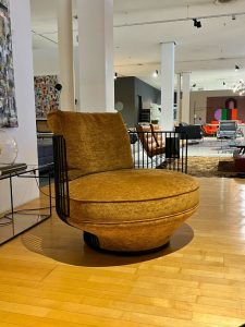 Mustard yellow round upholstered lounge chair with black metal frame in a modern furniture showroom on a wooden floor