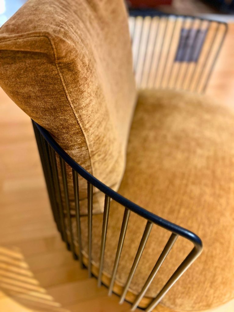 Close-up of a brown upholstered chair with a curved dark metal frame and vertical metal spindles.