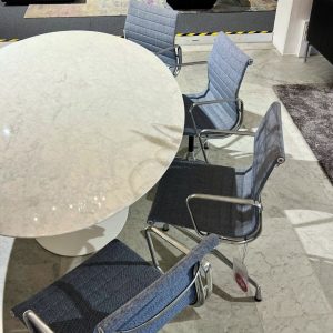 Round white marble table with four blue fabric swivel chairs in a modern showroom or office space.