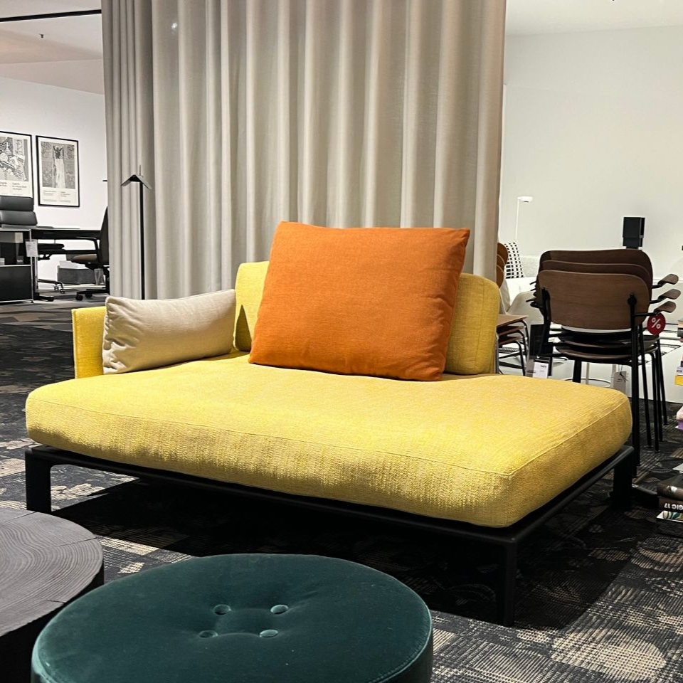 Yellow sofa with orange and beige cushions in a modern furniture showroom near a partition curtain.