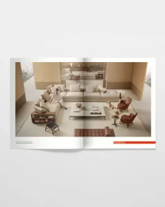 Two-page magazine spread showing a modern beige living room with a large L-shaped sofa, brown leather chairs, glass coffee tables, and a person seated on the sofa with a dog nearby.