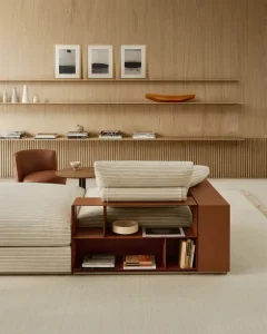 Modern living room with a cream-striped sofa, brown leather chair, and open shelving along the wall.