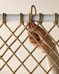 Close-up of a hand gripping a woven rope net attached to a horizontal bar.