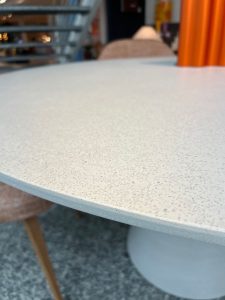 Close-up of a speckled white round table in an outdoor cafe, with blurred chairs and an orange curtain in the background.