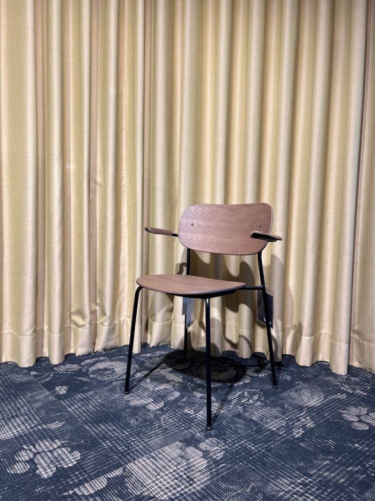 Wooden chair with curved backrest and black metal legs in front of beige curtains.