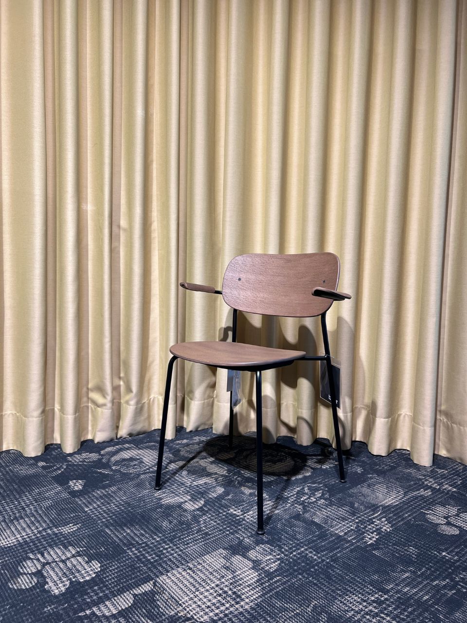 Wooden chair with curved backrest and black metal legs in front of beige curtains.