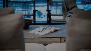 Open magazine on a marble coffee table in a cozy lounge, with blurred chairs in the foreground and a blue outdoor view beyond.