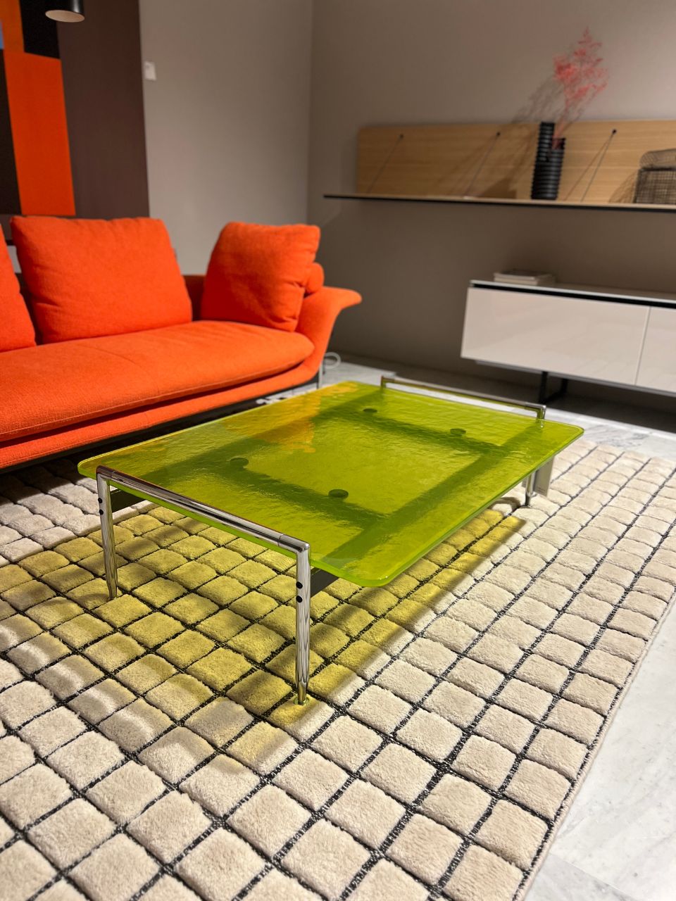 Modern living room with a bright lime-green glass coffee table and an orange sofa on a patterned rug.