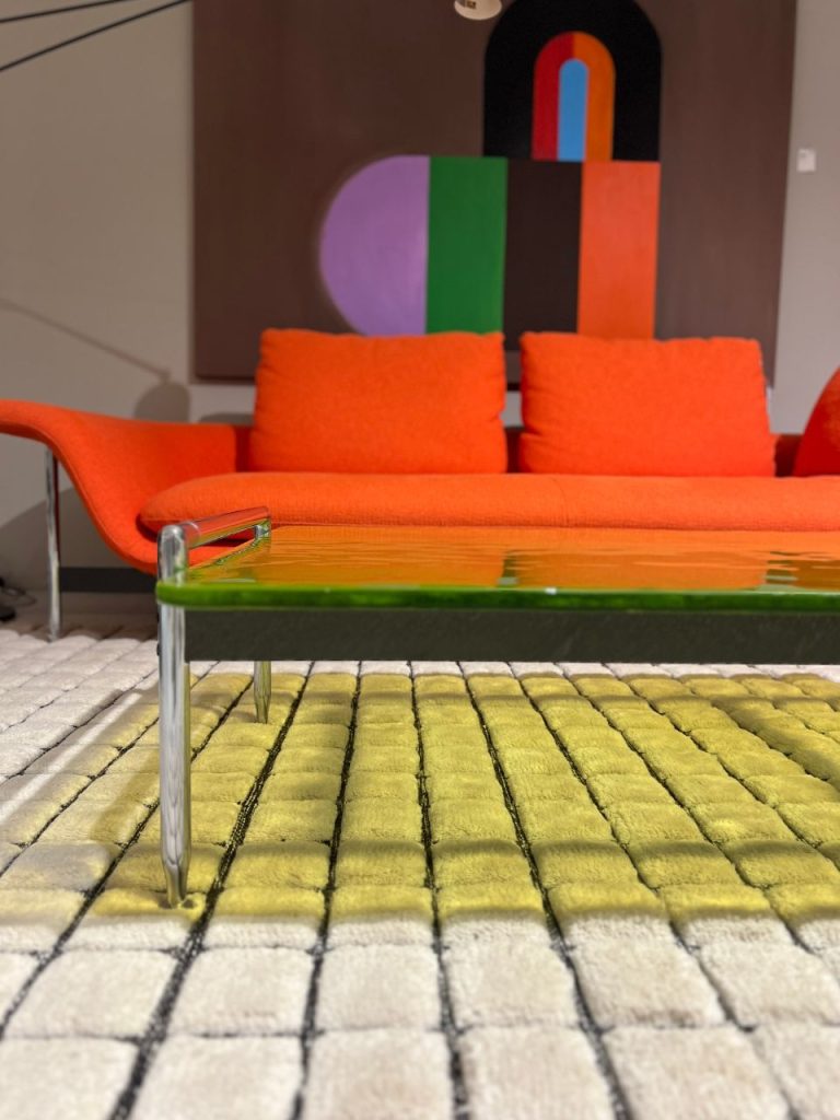 Bright orange mid-century sofa with matching cushions in a modern living room; abstract colorful wall art behind it.