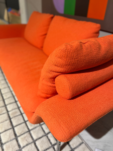 Bright orange upholstered outdoor sofa with matching bolster cushions on a tiled patio.