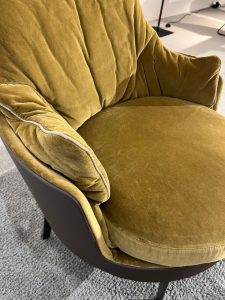 Mustard yellow velvet lounge chair with rounded cushions and a black curved base on a light gray carpet.