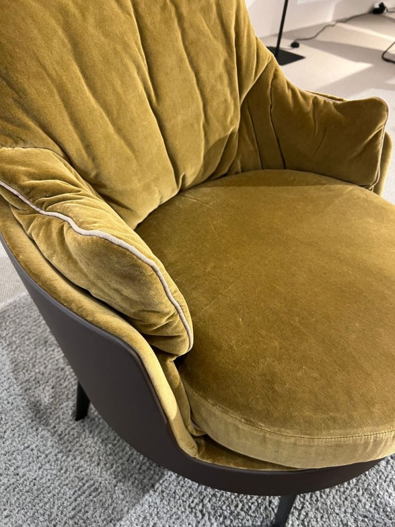 Mustard yellow velvet lounge chair with rounded cushions and a black curved base on a light gray carpet.