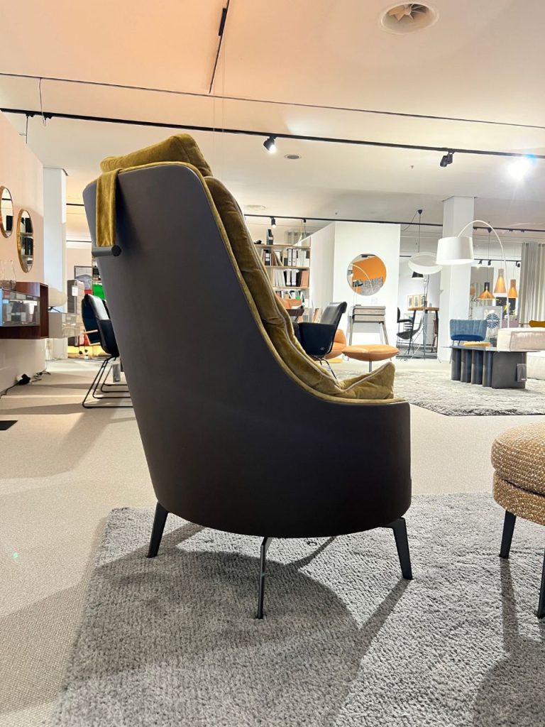 Dark curved lounge chair with a mustard blanket in a modern furniture showroom.