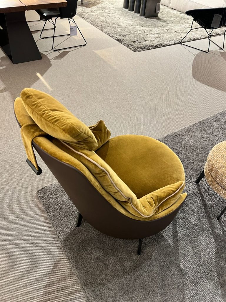 Mustard-yellow velvet lounge chair with a plush back cushion in a modern furniture showroom.