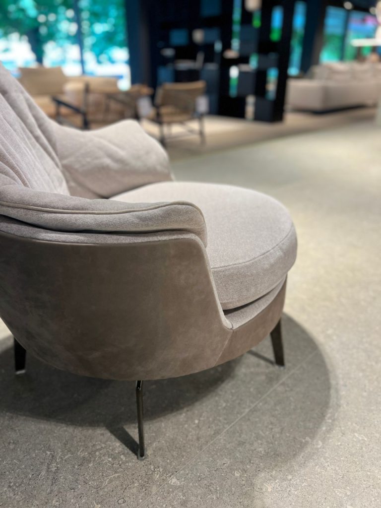 Gray curved upholstered lounge chair with metal legs, in a modern seating area.