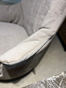 Close-up of a light-gray fabric sofa armrest with visible piping along the edge