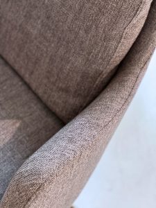 Close-up of brown textured fabric on a curved chair armrest and seat edge.