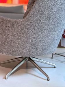 Close-up of a gray textured upholstered chair with a metal four-star base on a white floor in a showroom