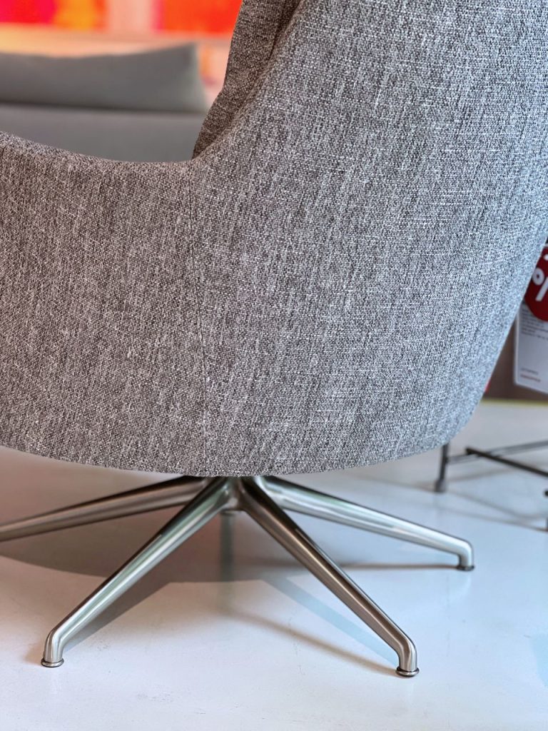 Close-up of a gray textured upholstered chair with a metal four-star base on a white floor in a showroom