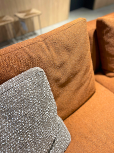 Close-up of a gray speckled cushion resting on an orange-brown sofa in a furniture showroom.