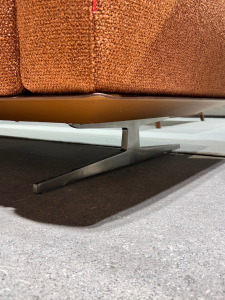 Close-up of a brown textured sofa with a gray metal sled-style leg on a gray floor