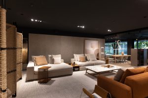 Modern showroom living room with beige sectional sofas, throw pillows, a marble coffee table, and a light striped rug.