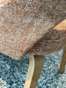 Close-up of brown speckled upholstered fabric draped over a light wood chair leg near a granite floor, highlighting the textured weave.