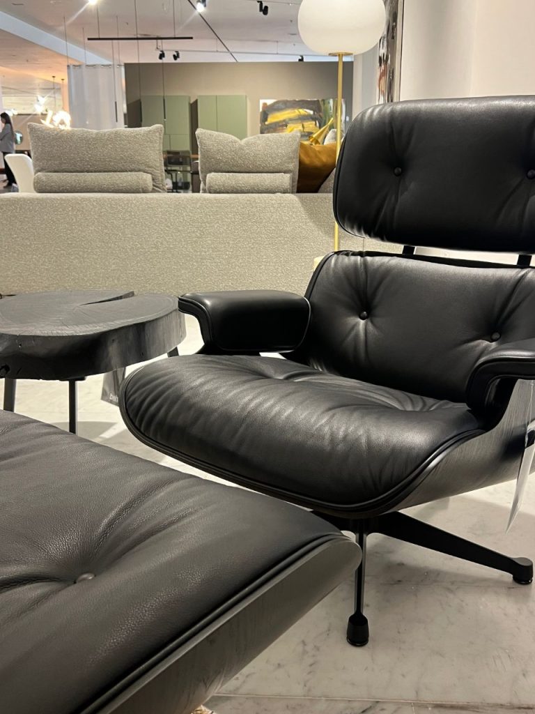 Black leather lounge chair with matching ottoman in a modern showroom, beige sofas and a marble floor in the background.