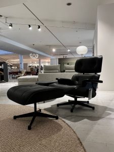 Black leather lounge chair with matching ottoman on a circular jute rug in a bright furniture showroom.