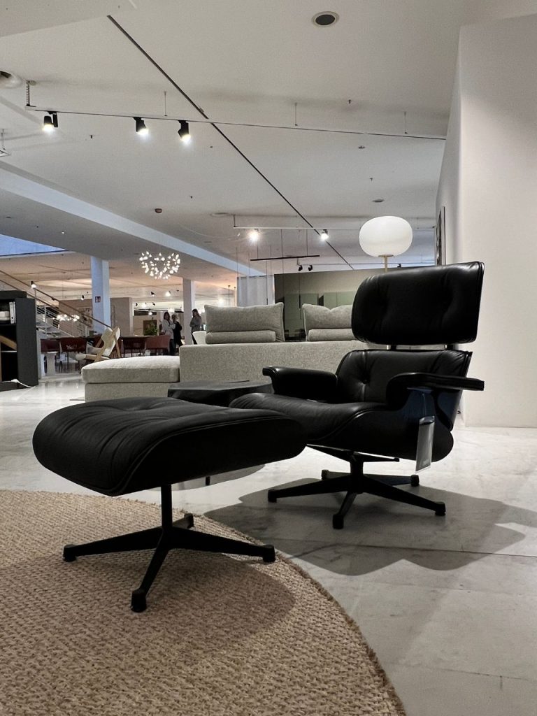 Black leather lounge chair with matching ottoman on a circular jute rug in a bright furniture showroom.