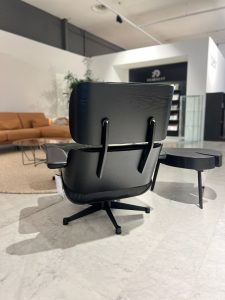 Black ergonomic office chair with a curved wooden back and cushioned seat on a wheeled base in a showroom.
