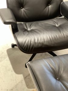 Close-up of a black leather office chair seat with button tufting and padded armrest on the left side.
