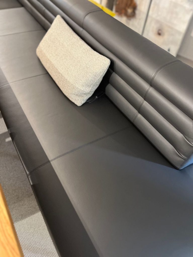 Black leather sectional sofa with a light fabric cushion resting against the backrest side panel.