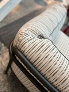 Close-up of a striped fabric armrest on a chair with a black metal frame, showing a tufted seam and curved contours.