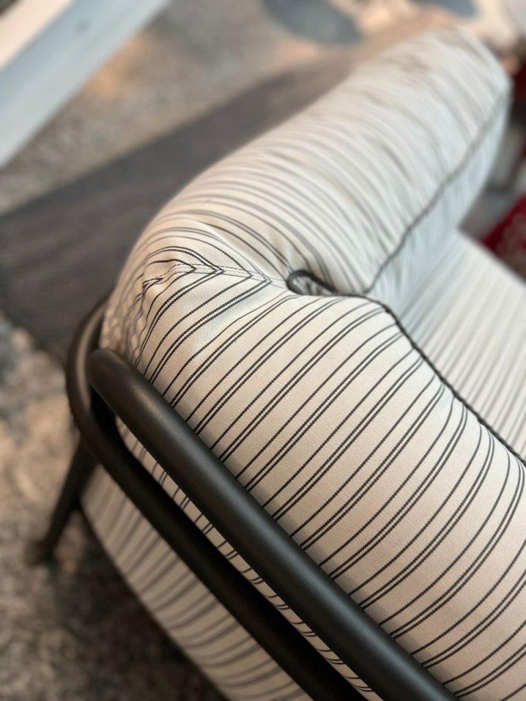Close-up of a striped fabric armrest on a chair with a black metal frame, showing a tufted seam and curved contours.