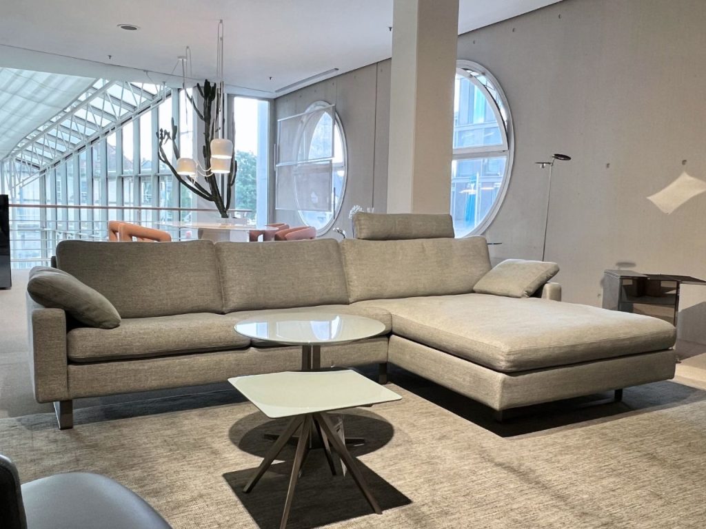 Modern grey sectional sofa in a spacious showroom with round windows and contemporary coffee tables nearby