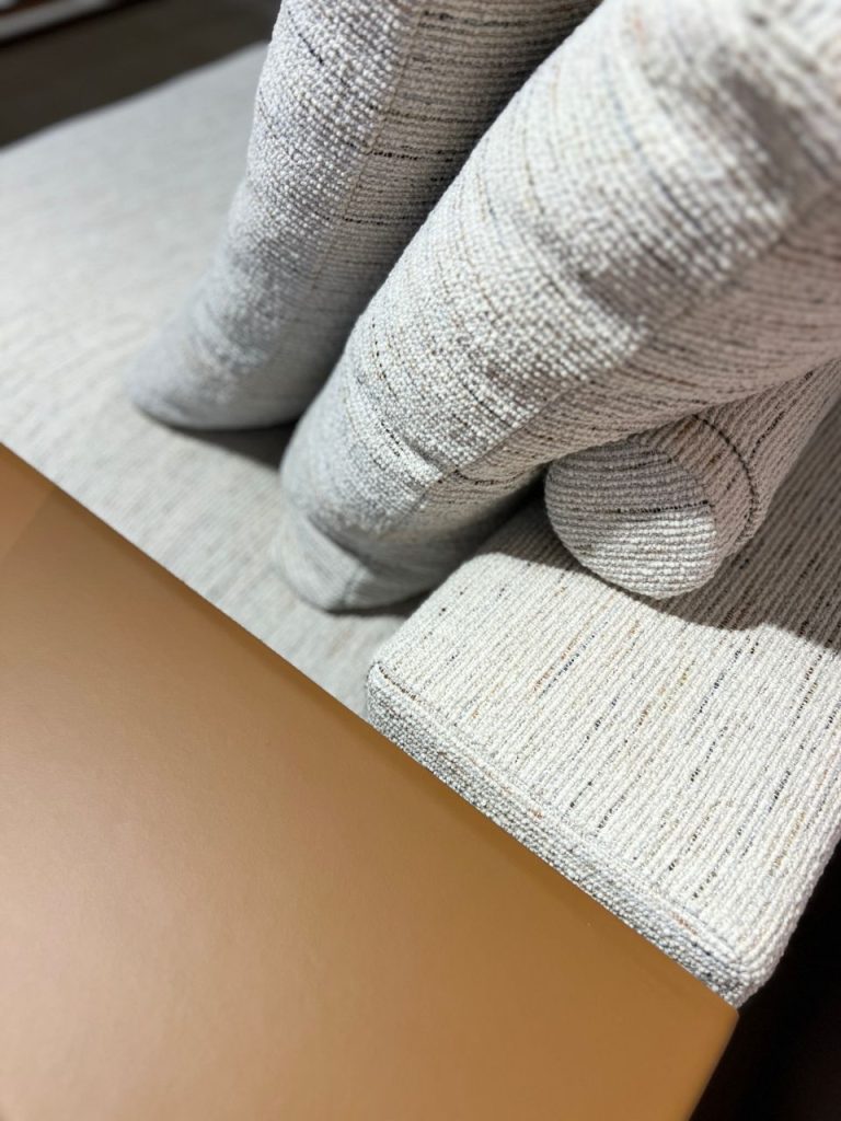 Close-up of light gray woven upholstery fabric with folds, resting against a tan surface.