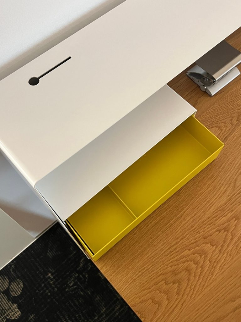 White cabinet with a bright yellow, two-compartment pull-out drawer on a wood desk.