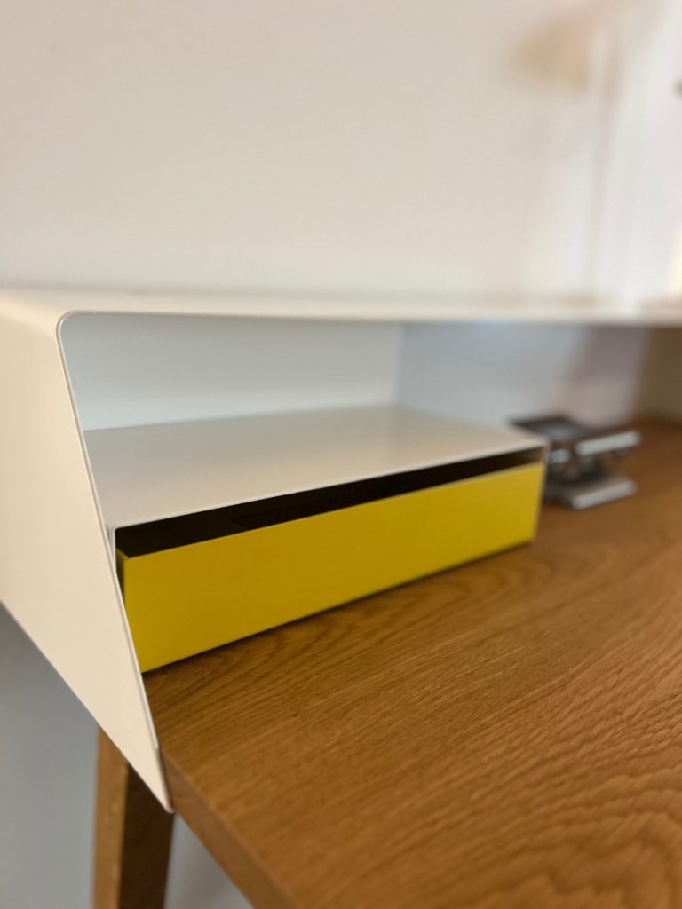 White angled desk shelf over a yellow storage drawer on a wooden desk surface.