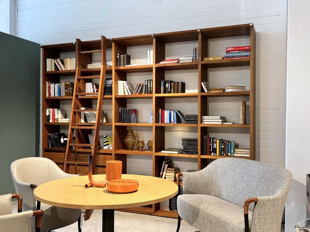 Round wooden table with orange decorative items in a cozy reading area, facing a tall wooden bookcase with a ladder1,]