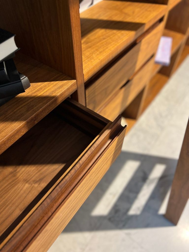 Close-up of a wooden dresser with an open lower drawer, showing smooth interior and visible grain in warm lighting.