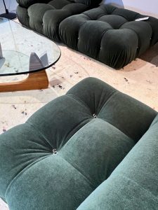 Two dark green tufted velvet sectionals arranged in a modern living room, viewed from above, with a round glass coffee table and a light speckled rug
