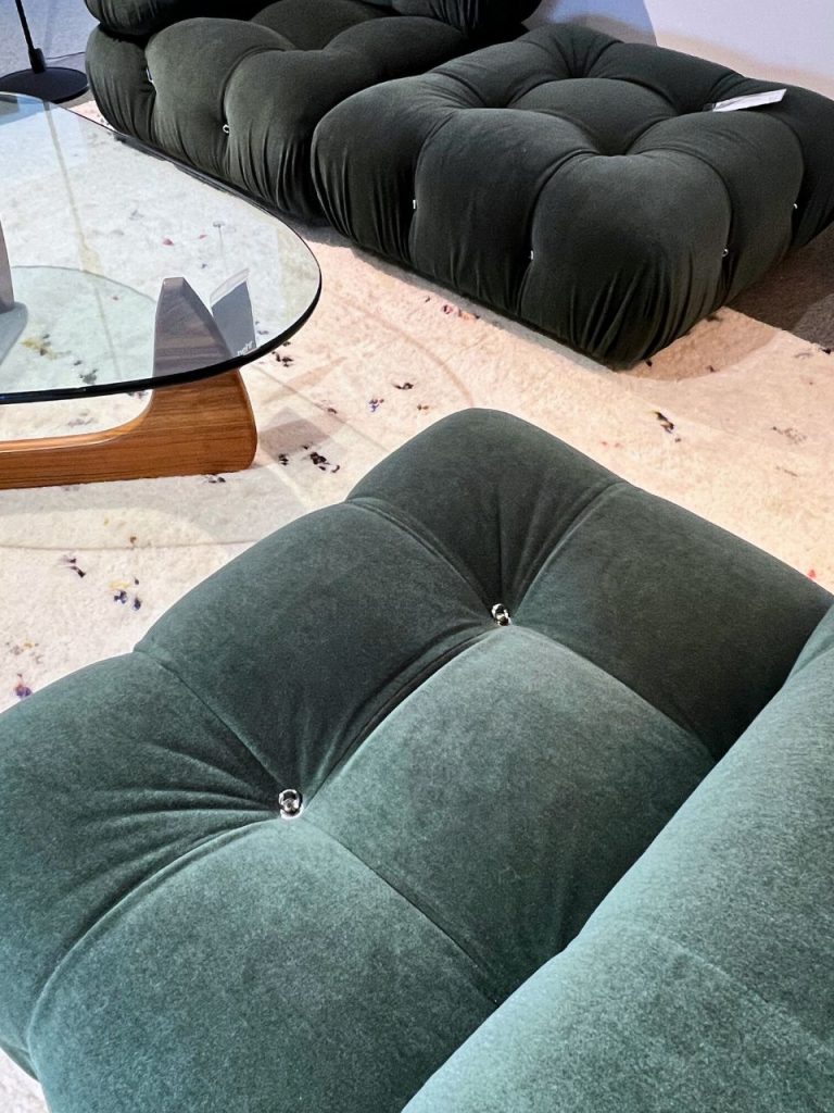Two dark green tufted velvet sectionals arranged in a modern living room, viewed from above, with a round glass coffee table and a light speckled rug