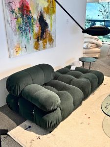 Dark green velvet tufted modular sofa on a light rug in a modern showroom with an abstract painting on the wall.