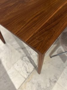 Close-up of a dark wood table corner and angled tapered leg on a light marble floor.