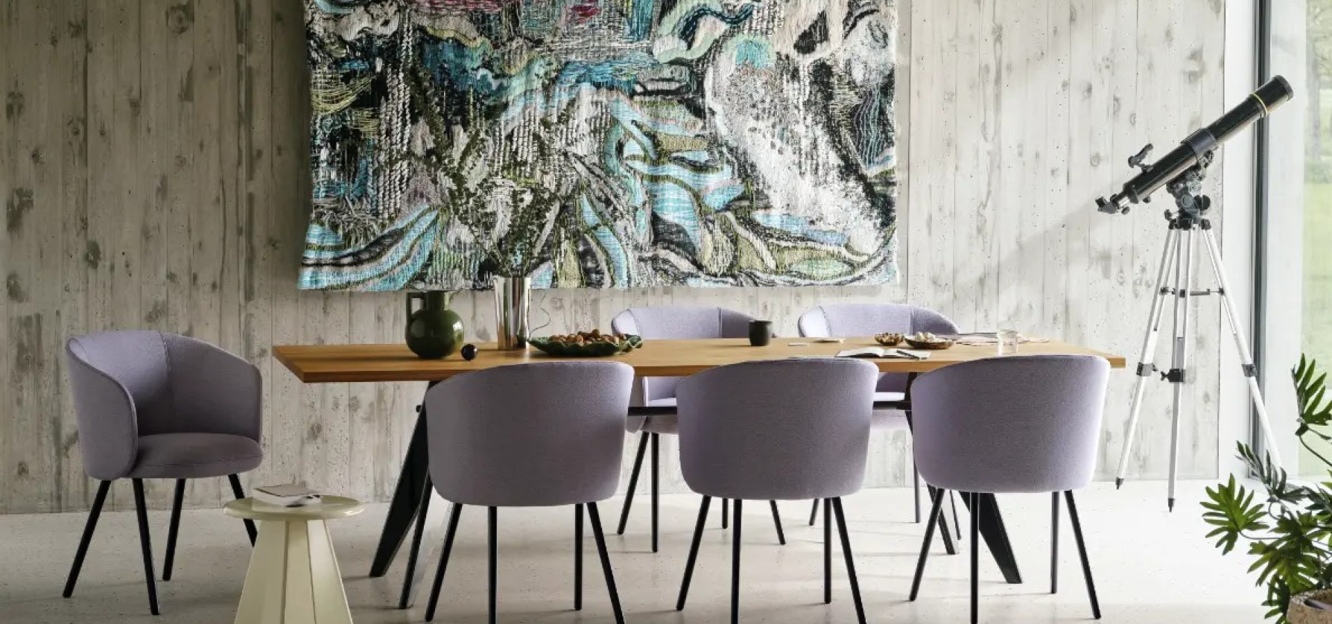Modern dining room with a wooden table and lavender chairs, large abstract wall hanging, and a telescope on a tripod by the window.